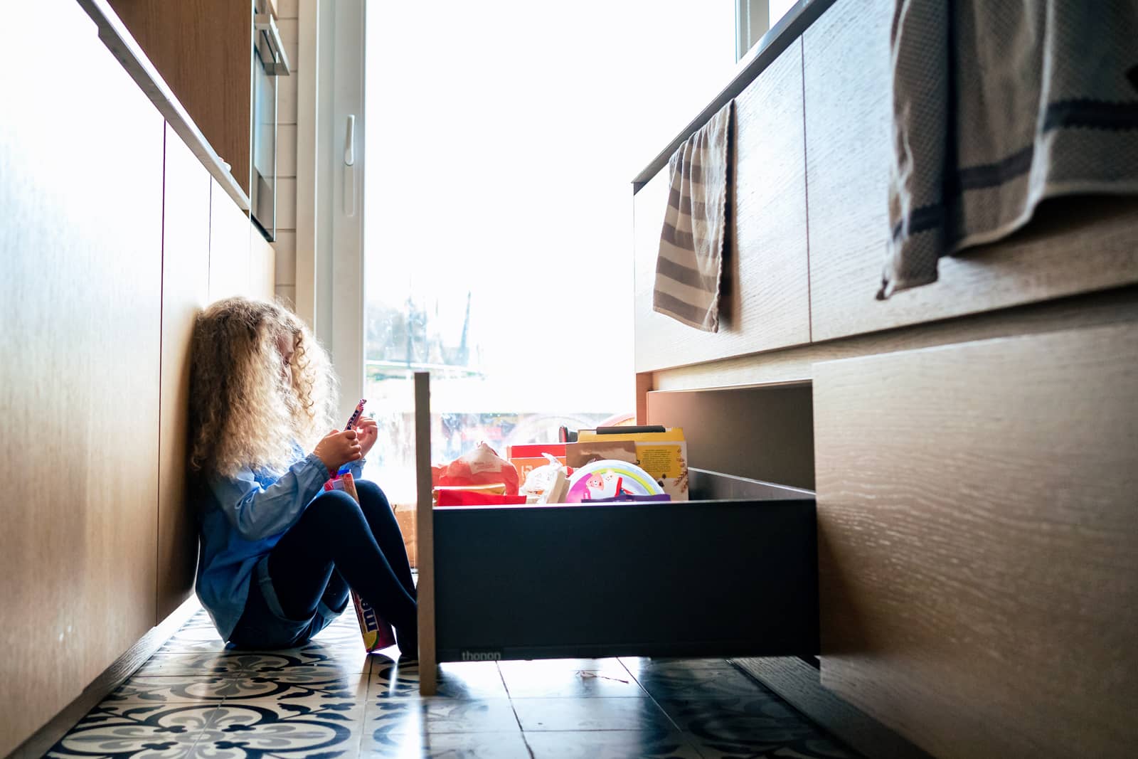 Petite fille assise devant un tiroir de cuisine ouvert avec des bonbons dans les mains.