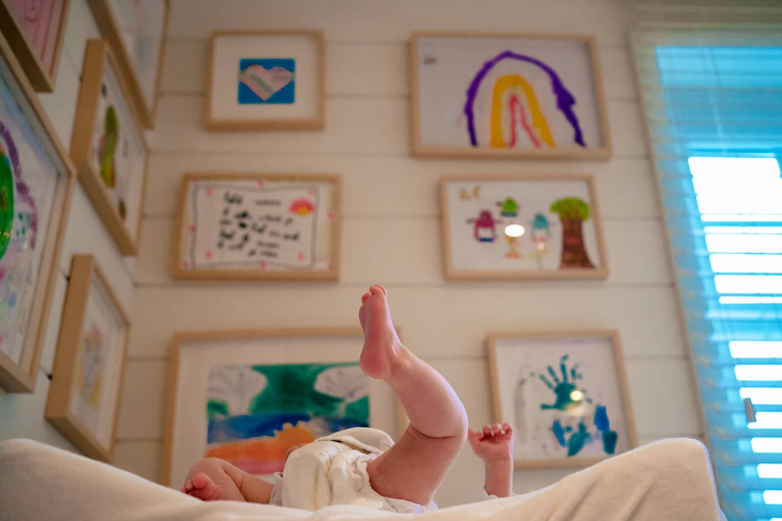 Les jambes d'un bébé au premier plan avec derrière un mur replis de dessin des enfants.