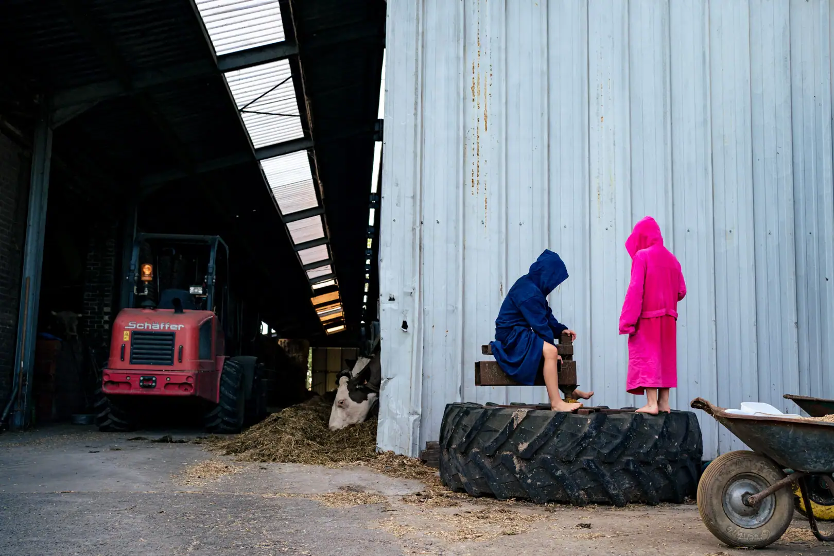 Deux enfants en peignoirs jouent sur un balançoire faite sur un pneu de tracteur au bord d'une ferme du Brabant Wallon
