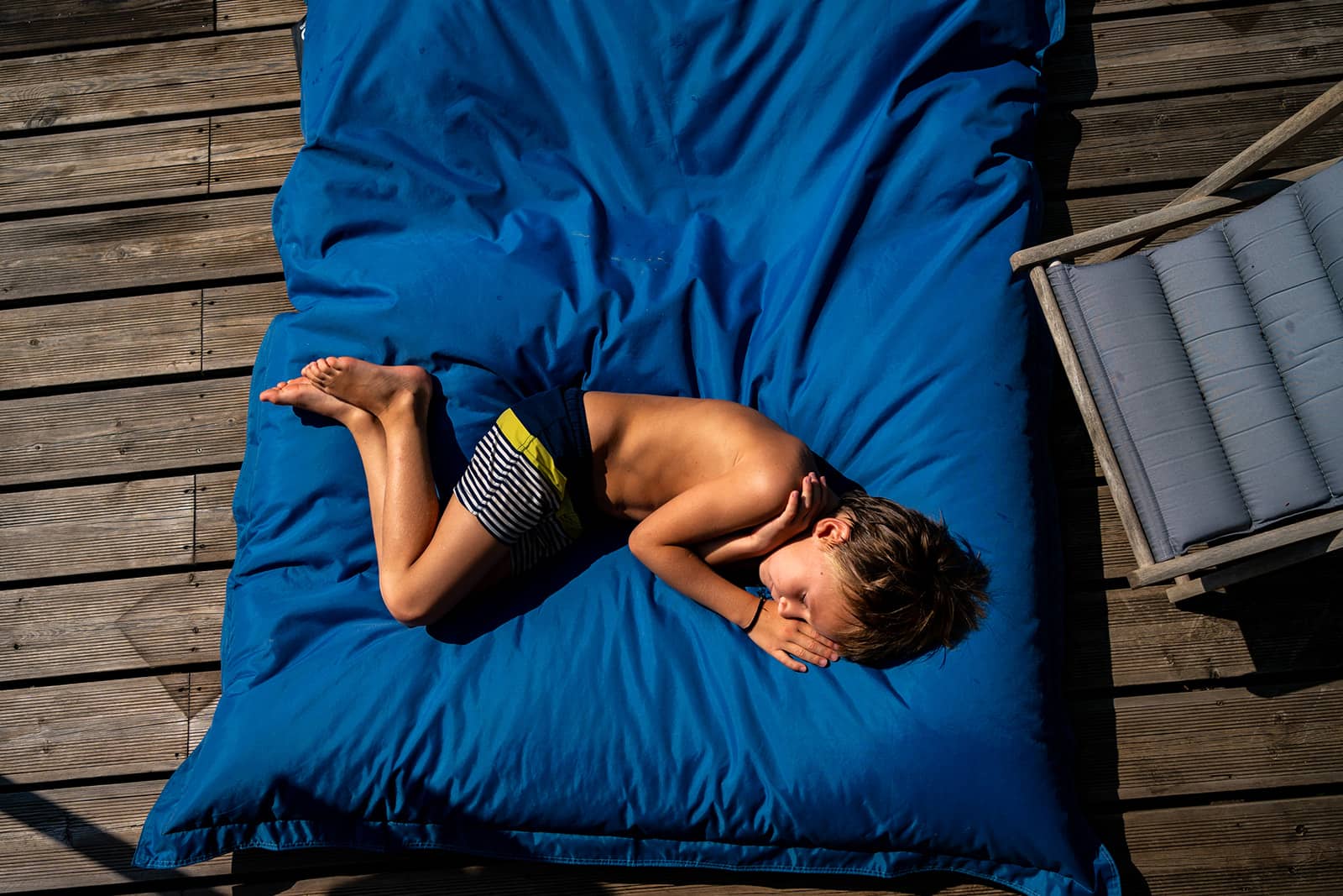 Jeune garçon dormant sur un gros coussin bleu au bord de la piscine.