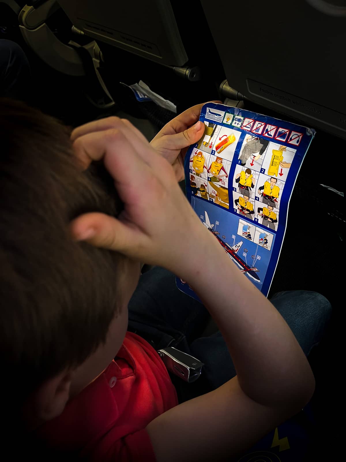 Un garçon se gratte la tête en lisant les instructions en cas de crash dans l'avion, reportage famille Brabant Wallon