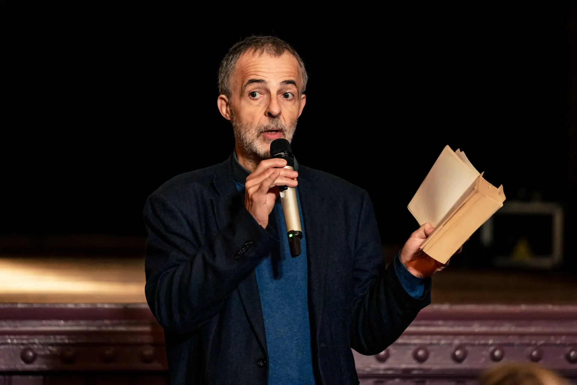 un orateur parle au micro avec un livre ouvert dans l'autre main au palais de Plume à Itttre