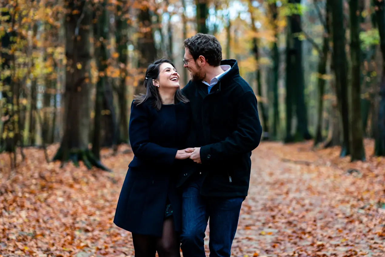 En couple marche sur un chemin recouvert de feuilles mortes dans le bois de la Cambre lors d'une séance photo de couple à Bruxelles 