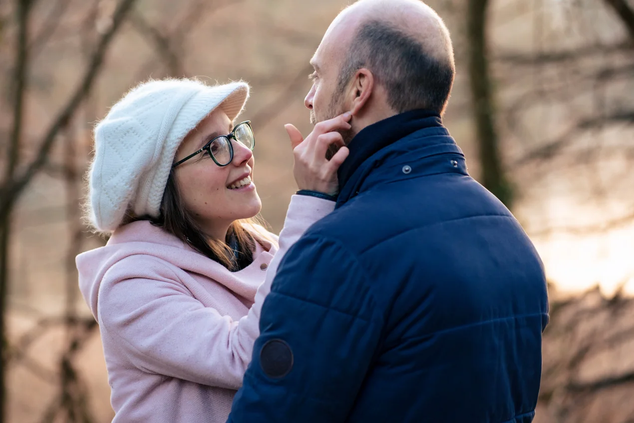 Une femme avec un bonnet regarde amoureusement caresse le visage d'un homme dégarni lors d'une séance photo de couple à Bruxelles