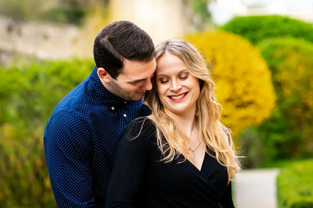 Un homme en bonnet se tient derrière une femme qui lui parle dans l'oreille alors d'une séance photo de couple à Luxembourg