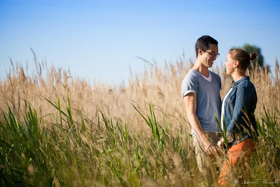 Un couple se tient face à face, les mains entrelacés dans des hautes herbes avec le soleil donnant un effet de contre jour.